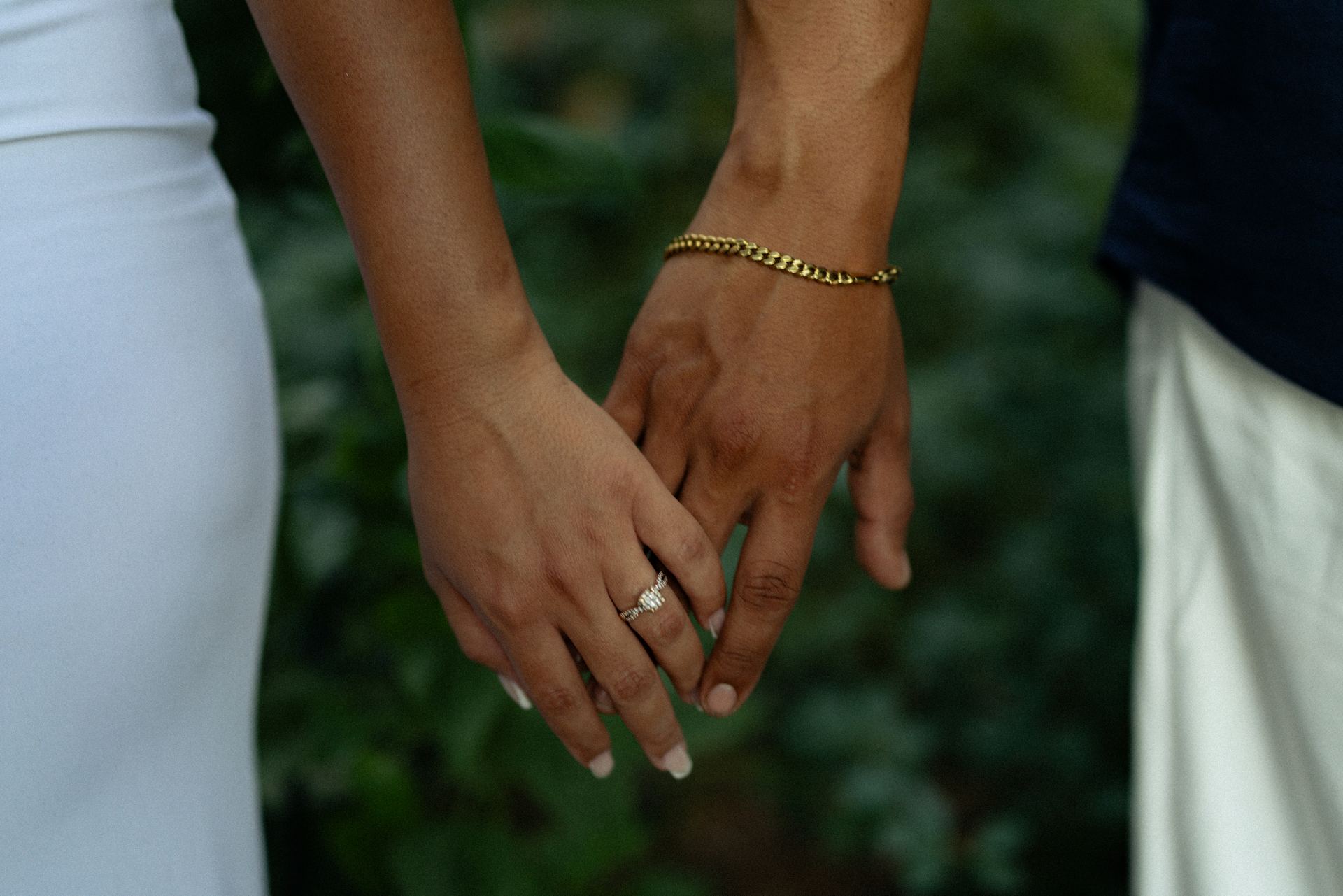 Two people holding hands, one wrist wearing a gold curb-chain permanent bracelet.